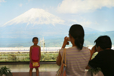 A young girl is photographed against a backdrop of Mount Fuji by her parents.