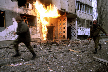 Chechen fighters move through the back streets of Grozny to their positions as a gas flame burns near the entrance to an apartment block after gas pipes were hit by shrapnel. Besieged residents later...