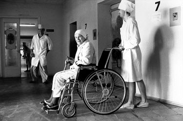 Nurse pushing an elderly patient's wheelchair down a hospital corridor.