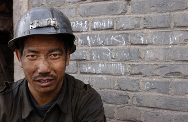 Just off shift, a coal miner rests outside the room where he has returned his headlamp. He is 36 and has left his wife at home in another province to work here and provide for his family.