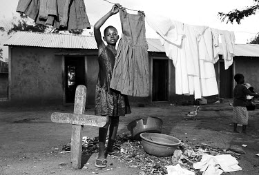 A young girl hangs her school uniform on the washing line next to her parents' graves. She is an AIDS orphan and looks after her younger siblings. Deaths from AIDS have increased the number of single-...