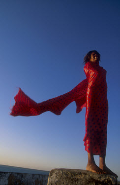 A woman in red stands against a deep blue sky.