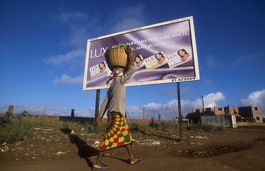 A poor woman with a heavy burden passes a billboard advertising Lux soap.