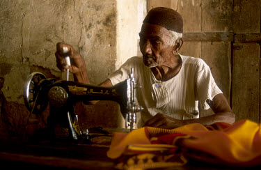 An old tailor works on a pedal-operated sewing machine.