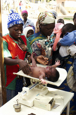 Women bring their children to a health station for vaccinations and a general check-up. Here a baby is weighed.