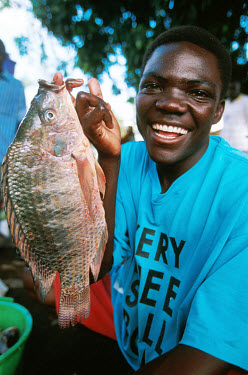 Man holding a freshly-caught tilapia fish brought ashore at Dunga beach on Lake Victoria.