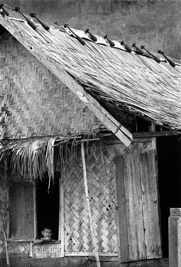 A boy at the window of his home. Mortar bombs and recoilless rounds tied tail-to-tail are used to help hold down the thatched roof in storms. Two of the bombs are still fused. Decades on, Laos is stil...