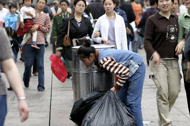 An impoverished woman searching for recyclable bottles in a rubbish bin on Nanjing Road, the main shopping district, during the May holiday weekend.