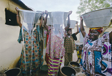 Women pour water from containers on their heads after collecting water at the local pump where it is sold by 20 litre buckets or the barrel. The money is managed by the community and used to pay salar...