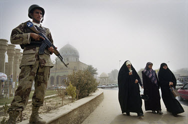 Three veiled women walk past an Iraqi soldier in Firdous Square. Since the US invasion an increasing number of women have been wearing the hijab. Mobile phones (as used by the woman on the left) are a...