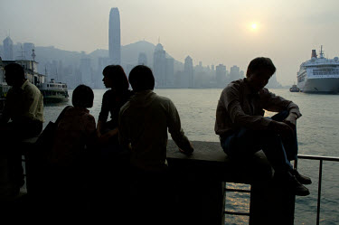 People chatting on the Kowloon waterfront at dusk, with Hong Kong island across the harbour, including Two International Finance Centre (415m), the city's tallest skyscraper, completed in 2003 on recl...