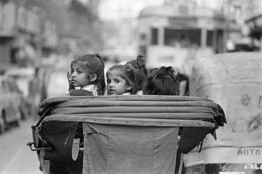 Middle class children in uniform being taken to school on a man-pulled rickshaw.