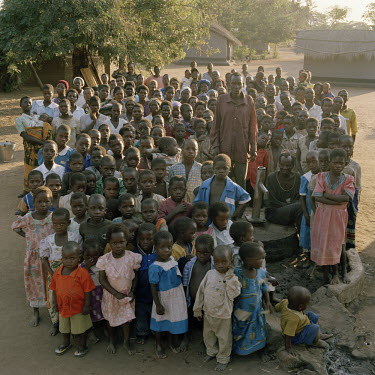 A group portrait of the residents of Dickson village. To the left of the pump, standing, is the village headman; to the right of the pump, sitting, Anderson Isimu (65), maimed by leprosy since 1973, o...