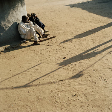 Male villagers rest after work. The shadow on the ground is made by a nearby tobacco packaging installation.   The village of Dickson contains 55 households and some 300 inhabitants. In 2005 photograp...