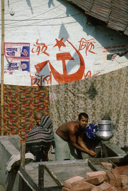 Slum dweller washing his hands at a communal water tap, with the hammer and sickle emblem on a wall behind. The state of West Bengal has had an elected communist government for 25 years.