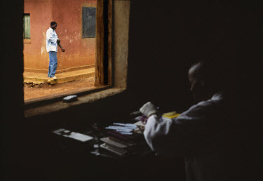A patient walks past a window, having had an HIV test at Kibayi Health Centre, while a health worker develops a tests in a locked room.