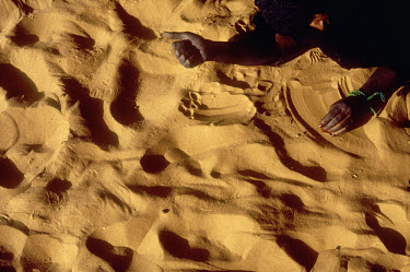 An elderly Moorish nomad woman draws patterns in the sand.