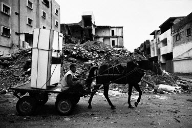 An inhabitant of a nearby destroyed tower block transports his fridge by horse and cart, having been forced to move away to live with friends and family.