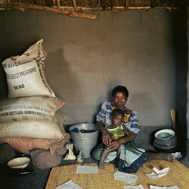Mazire Odadi (20) sits in her house with her son Thokozani (2), beside sacks of fertilizer.  Her husband rolls cigarettes using the pages of an exercise book.