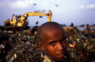 Twelve year old Kamal stands in front of a hydraulic digger on the Kajla rubbish dump where he is a professional scavenger.  He has never been to school, but earns his money by selling waste paper and...