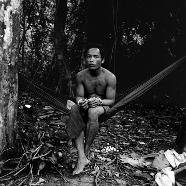 A handcuffed poacher sits in a hammock waiting to be questioned by members of the National Cambodian Forestry Security service.  He was arrested while operating as part of a poaching team in Bokor Nat...