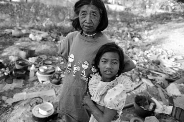 Homeless mother, wearing a Peanuts T-shirt works on a rubbish tip with her daughter.  They scavenge the dump collecting recyclable items for resale.