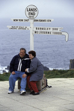 Visitors to Britain's southernmost point sit under a signpost marking relative distances to other parts of the world.