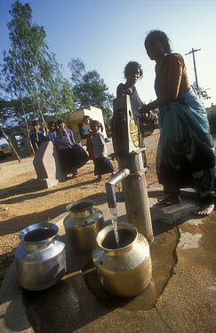 Women collect water in brass containers from a hand pump well.  The water system in the village is being upgraded to a piped water scheme as part of a local government pilot project.