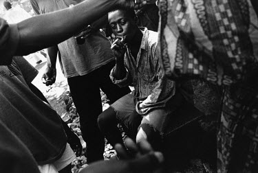 17 year old Febbah, a former child soldier, sits smoking with his friends and family after returning to Freetown.