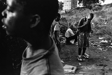 Former child soldiers gather to drink and smoke drugs in a clearing in a rubbish dump.  21 year old Moses (smoking) used to work as a radio operator during the siege of Huambo.