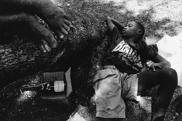 A child of the Interahamwe (meaning Those Who Stand Together or Those Who Fight Together), sleeps under a tree after drinking spirits.  The Interahamwe was the largest of the militia groups formed by...