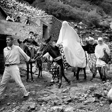 A veiled bride is led on a horse to her wedding ceremony as villagers follow.