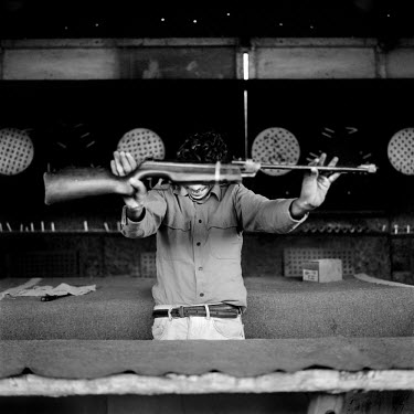 Stallholder at a fairground shooting gallery holding a rifle.