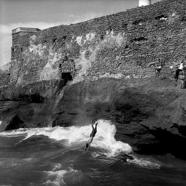 Boys dive off rocks into the sea outside the city wall.