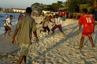 Mixed race young men playing football on the beach at sunset next to the Indian Ocean.
