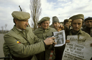 A group of soldiers point a gun at a picture of the former leader of the Communist Party of Romania, Nicolae Ceausescu, labelled 'Criminal'.