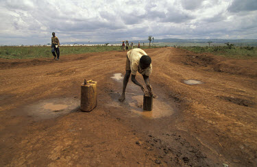 Rwandan refugee collecting water from a puddle in the road near the Benako refugee camp, which shelters refugees fleeing the genocide.