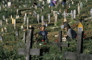 Child and mother visiting the father's grave in a graveyard.