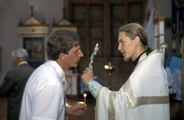 A member of the congregation kisses a silver cross held by a Priest duing a Russian Orthodox church service.