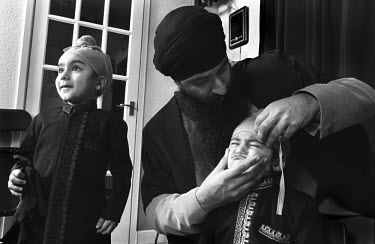 A father arranges his son's turban as the Sikh family get ready for an outing from their home in Pudsey.
