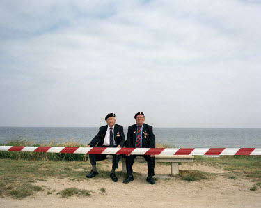 Two British veterans of World War II (WW2) sit on a bench on Gold Beach during the annual D-Day commemoration.  Gold Beach was one of the two British landing beaches on D-Day on 6th June 1944.  The No...