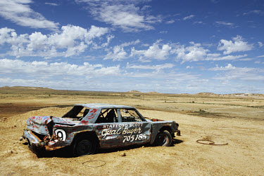 A wrecked and abandoned car painted with the sign 'Opal Buyer' in the desert near Coober Pedy. The area is the capital for opal mining in Australia.