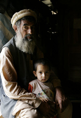 Muhannad Ifaq (55) sits with his son inside their shelter in Pokal. Muhannad's wife died when their home collapsed as an earthquake struck the region. One year later, thousands of people are still wai...