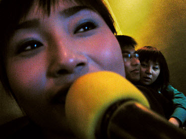 A young woman sings into a microphone at a karaoke bar where young sex workers solicit clients. Many of the karaoke bars in China run brothels. Although prostitution is illegal and both the women and...