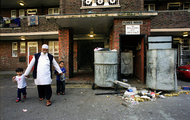 A Muslim family pass a pile of litter scattered around the rubbish bins outside the flats on Ocean Estate in Tower Hamlets.