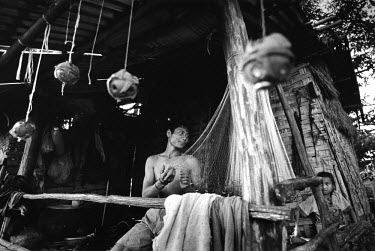 Deactivated BLU-42/B antipersonnel mines, remnants of the Vietnam War, hang next to a young fisherman as he mends fishing nets outside his home. The youth explains: 'I took them apart because we were...