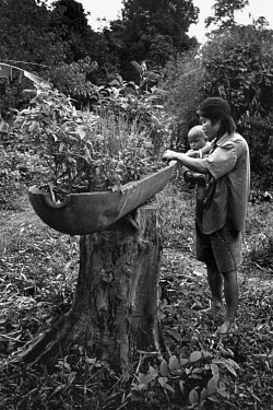 Thong holds his baby son, Nek, while weeding the vegetable plants that he grows in the casing of a salvaged cluster bomb, a remnant of the Vietnam War. Local ingenuity has transformed the detritus of...