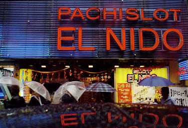 People with umbrellas passing outside an arcade while walking in the rain.