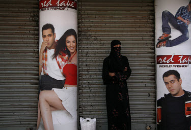 A Muslim woman stands in front of advertising for Western-style fashions outside a local store.