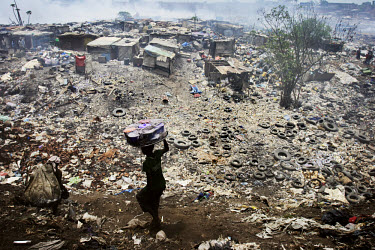 A vendor carrying food on his head descends on a village at the Olusosun landfill site. The Olusosun dump is Nigeria's largest trash heap comprising over 100 acres of garbage and is believed to be the...